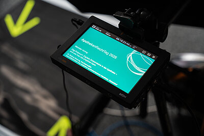 Kamera-Monitor zeigt türkisnen Bildschirm mit weißem Titel "ApothekenRechtTag", darunter mehrere Listenpunkte und eine stilisierte Kreisgrafik.