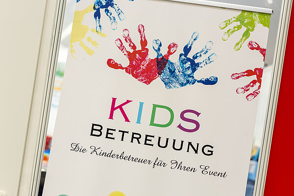 Zu sehen ist ein buntes Plakat mit farbigen Kinderhänden und der Aufschrift KIDS Betreuung