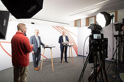 Behind the Scenes: Dirk Di Filippo, Hubert Ortner und Johannes Bauernfeind. Flankiert wird die Szene von Kamera- und Lichtequipment.