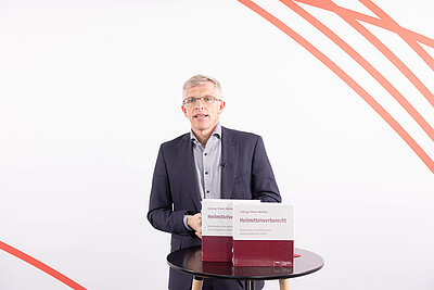 Professor Dr. Elmar J. Mand steht referierend hinter einem Stehtisch. Auf dem Tisch zwei Ordner "Heilmittelwerberecht"