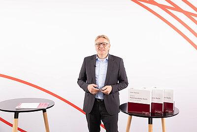 Dr. Volker Lücker referiert stehend zwischen zwei Stehtischen. Auf dem rechten Tisch stehen drei Ordner "Medizinprodukte-Recht"