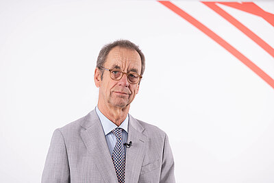 Porträt von Dr. Christian Rotta er schaut freundlich in Richtung der Kamera. Weißer Hintergrund mit rotem Streifenmuster.